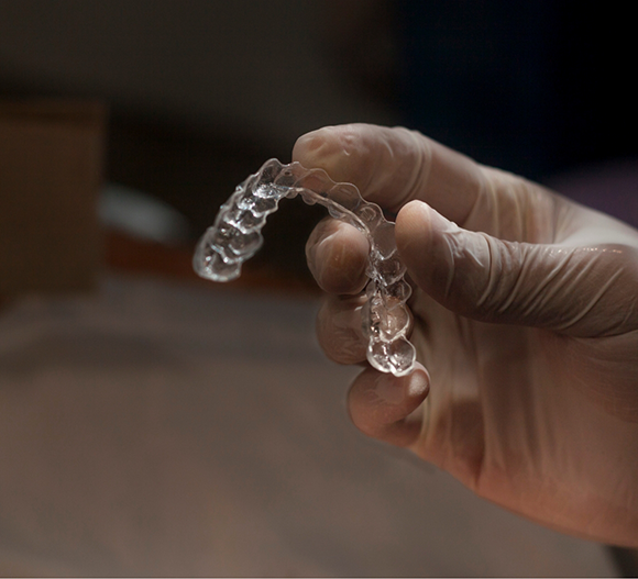 Gloved hand holding a clear retainer