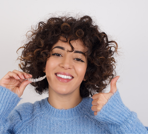 Woman holding a clear aligner and giving a thumbs up