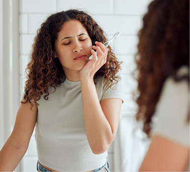 Woman with a toothbrush holding her cheek in pain