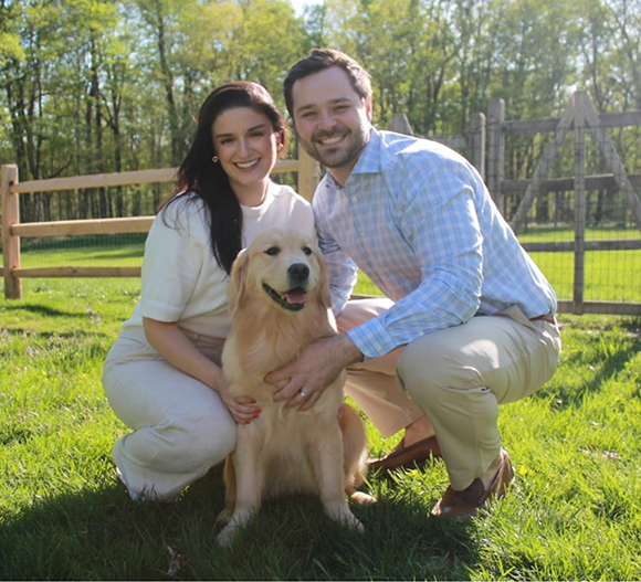 Doctor Brown smiling with his wife and golden retriever in their yard