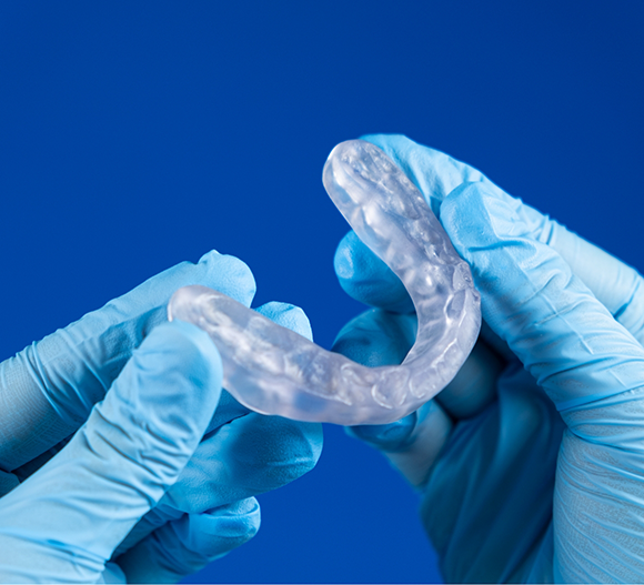 Gloved hands holding a clear nightguard