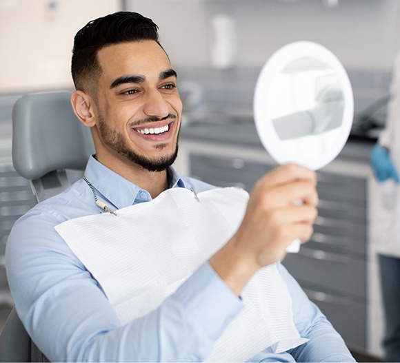 Man in the dental chair admiring his smile in a mirror