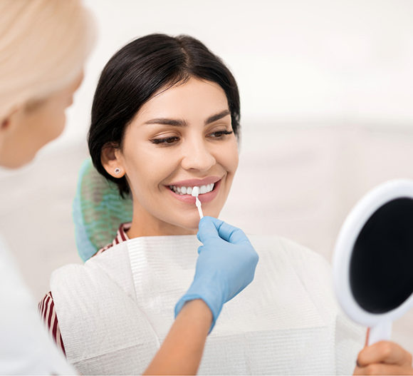 Dentist holding a veneer in front of a patient's smile