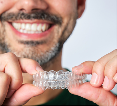 Smiling man holding two clear aligners