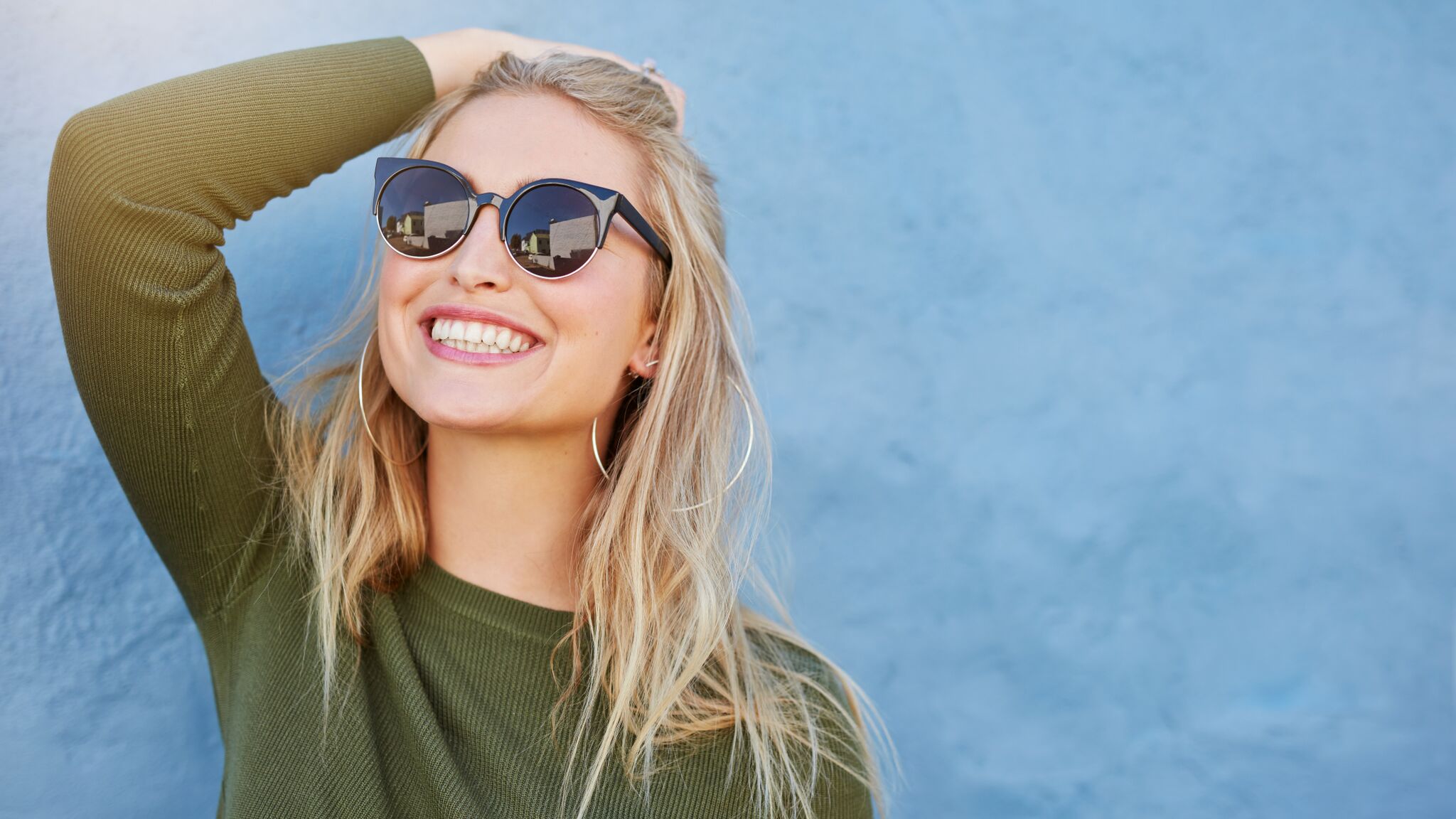 Woman with sunglasses smiling after seeing her cosmetic dentist.