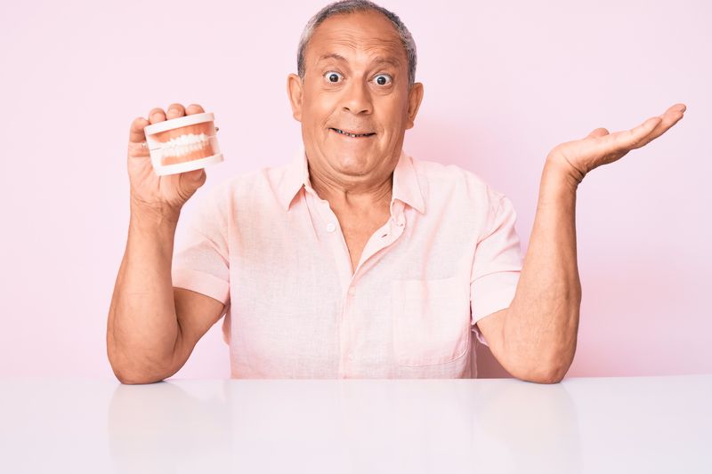 Mature man holding dentures.