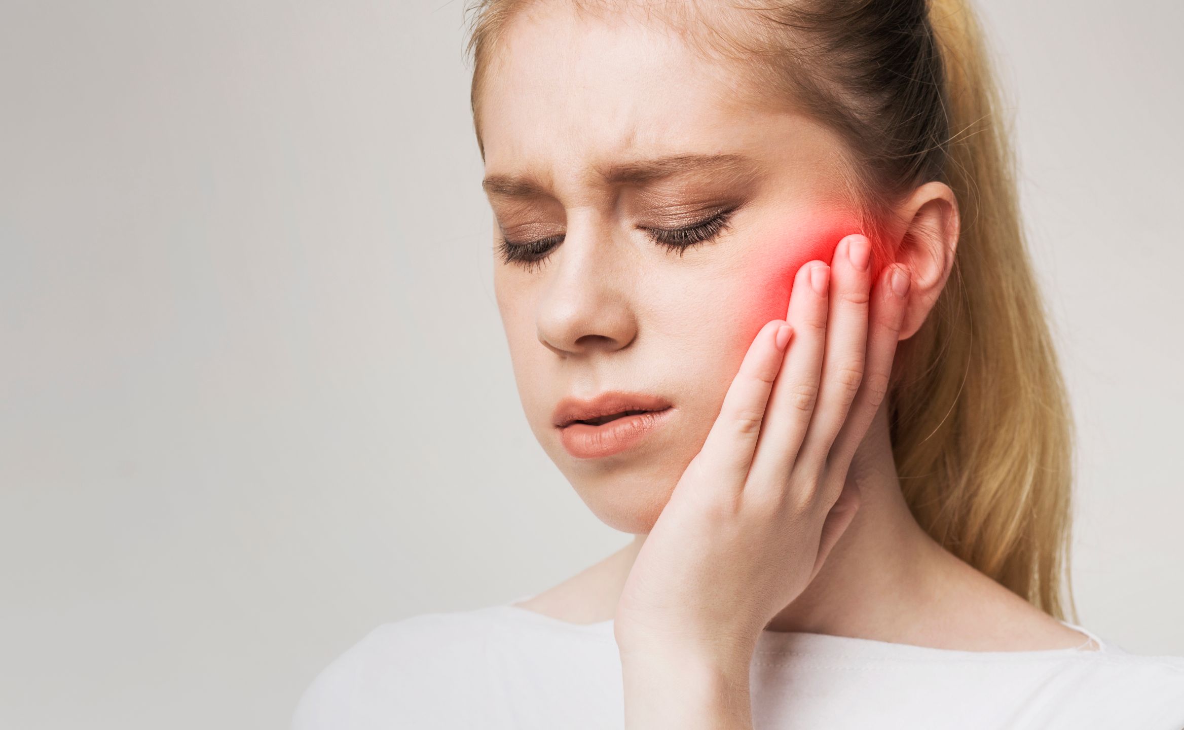 Woman holding hand to her red swollen jaw in pain.