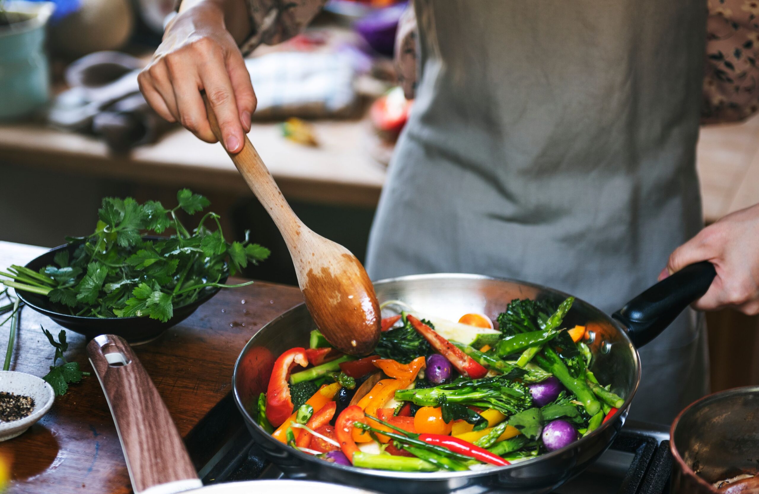 Closeup of someone in gray apron sautéing vegetables.