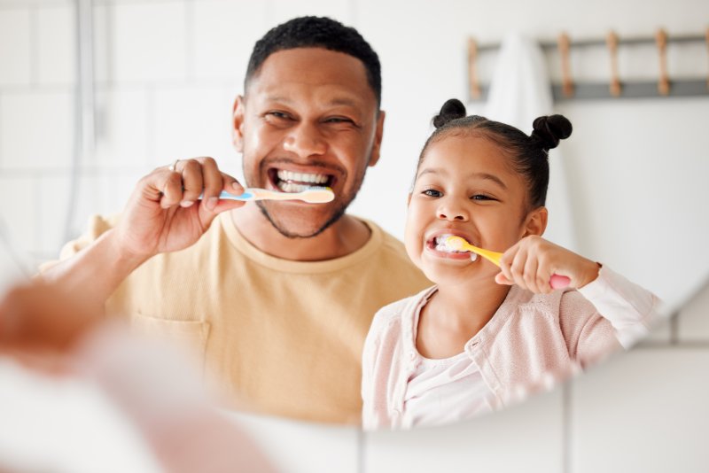 Father and daughter brushing their teeth.