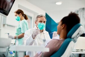 Dentist treating patient with team member in background.